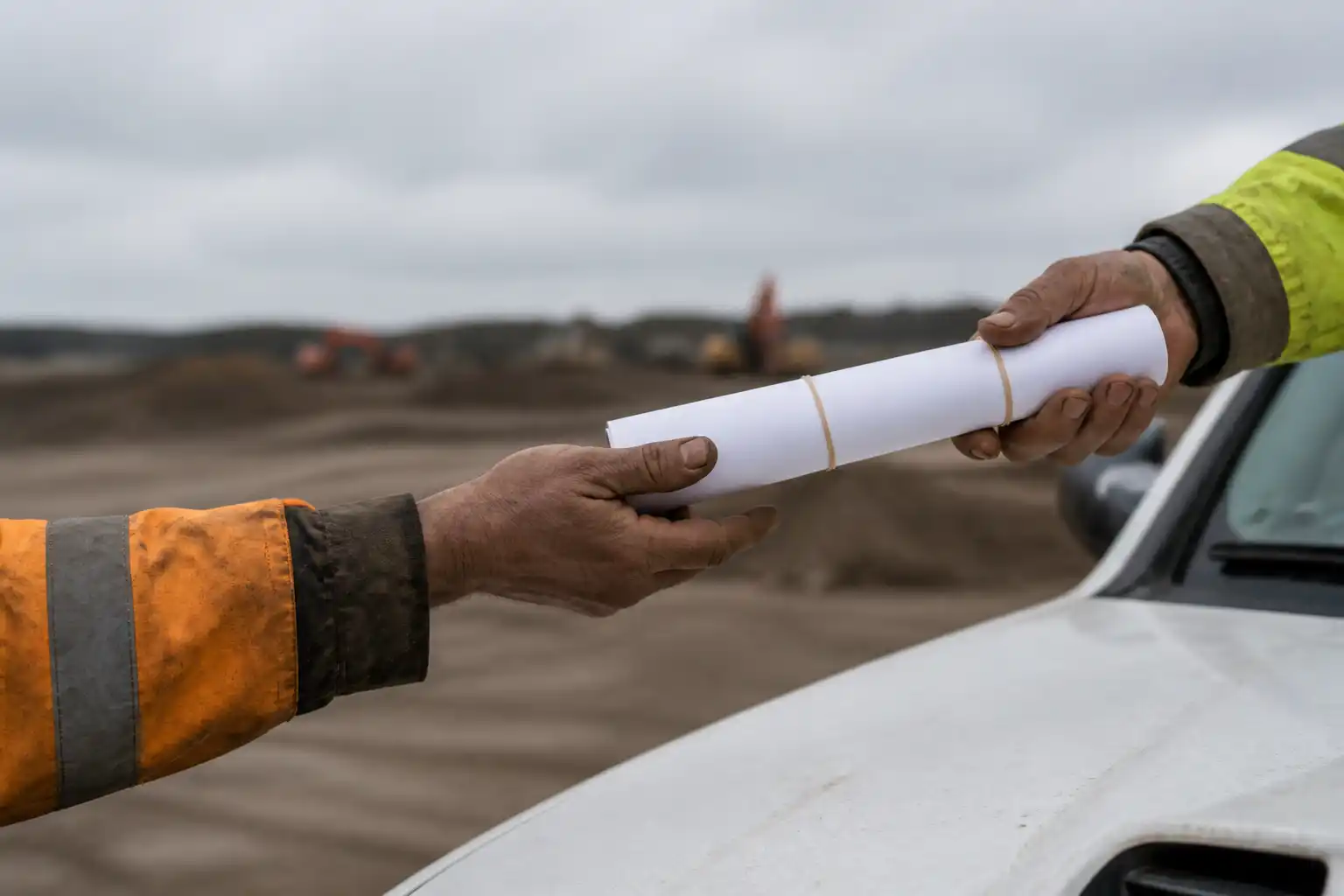 A rolled set of drawings passing from one pair of work-worn hands to another on a construction site